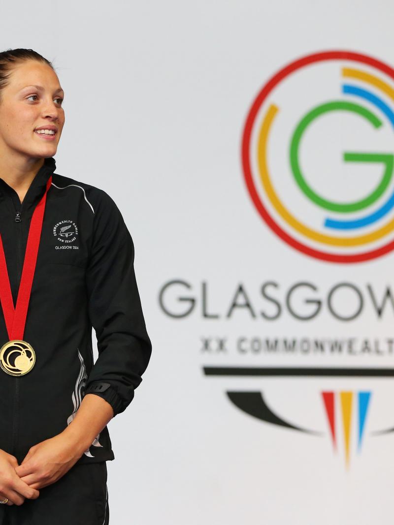 Women in training suit stand in front of a wall with the Glasgow 2014 logo
