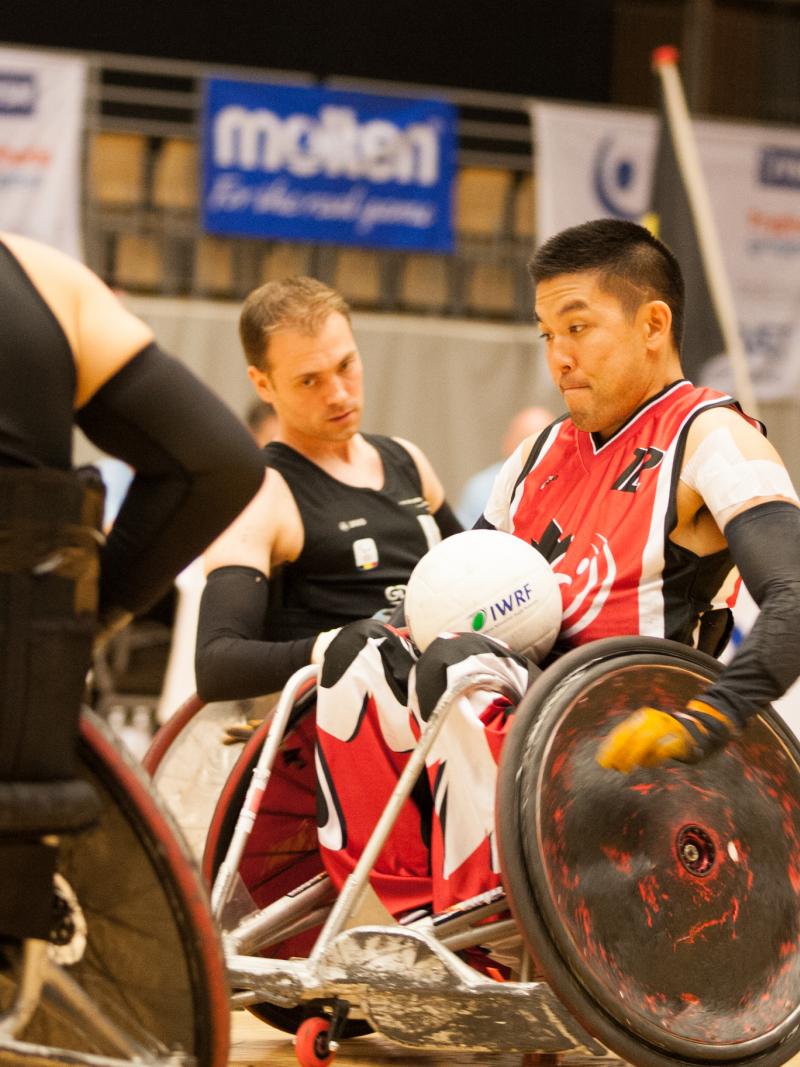 Man in a wheelchair with a ball in his lap going forward.