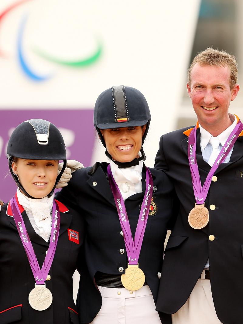 Two women and one man in dressage uniforms standing on the medals podium.