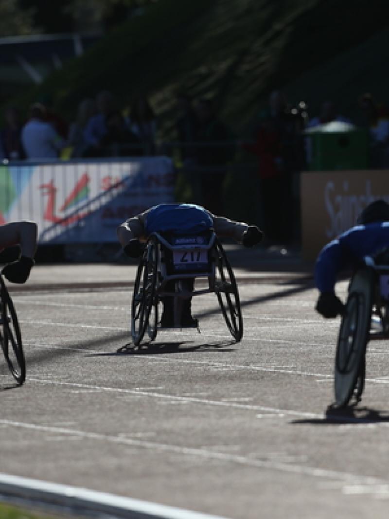 Wheelchair athletes race on a track, photographed from the back