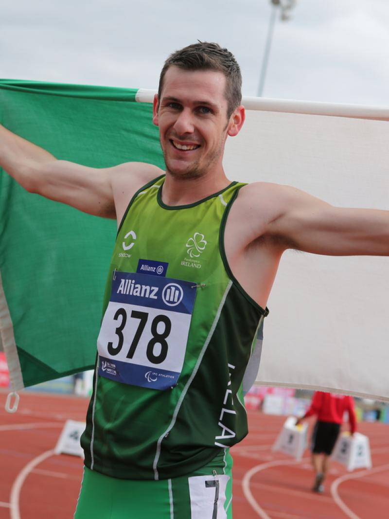 Man in green shirt holding an Irish flag and smiling to the camera
