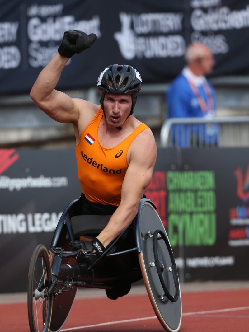 Man in racing wheelchair holding a Dutch flag, celebrating