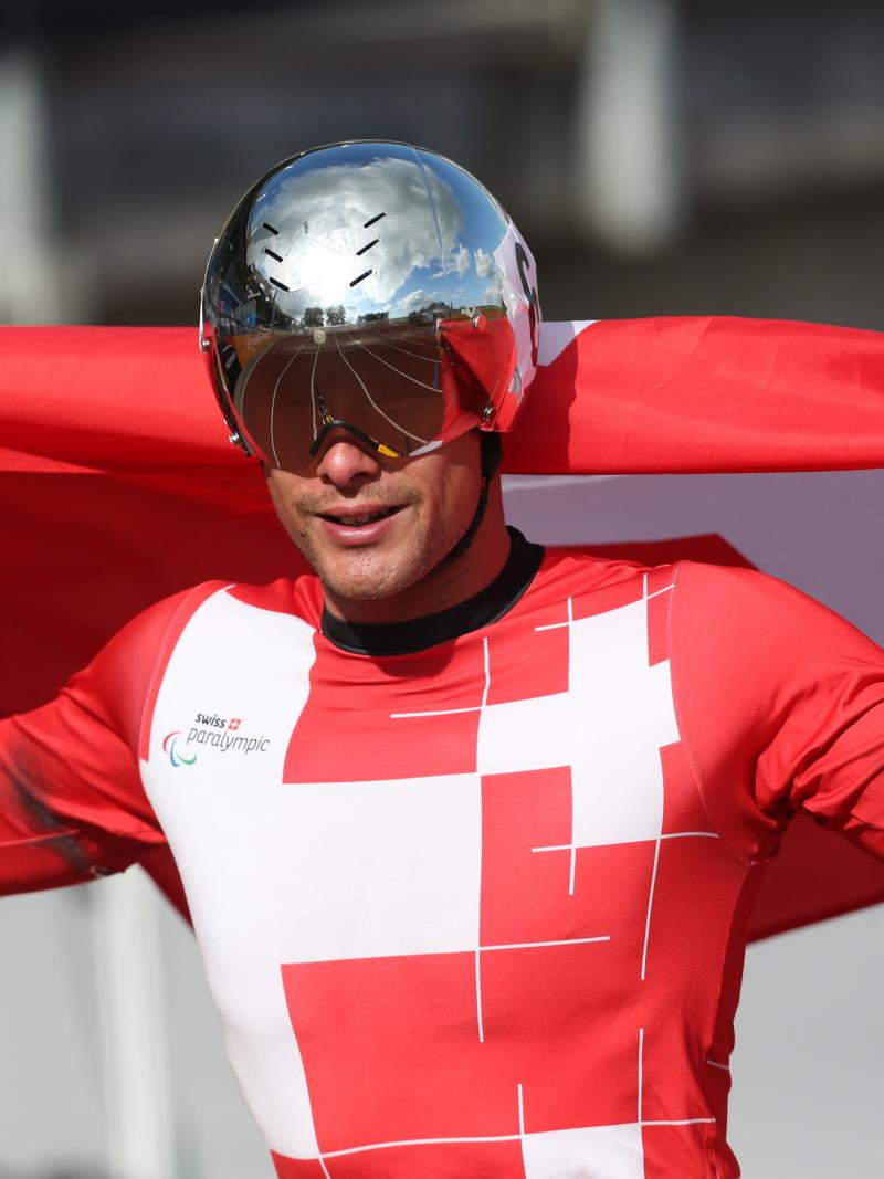 Man in red jersey with silver helmet and a Swiss flag smiling to the camera