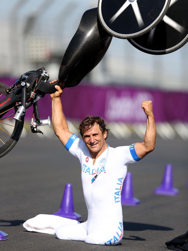 Man on a track holding a handbike above his head and smiling