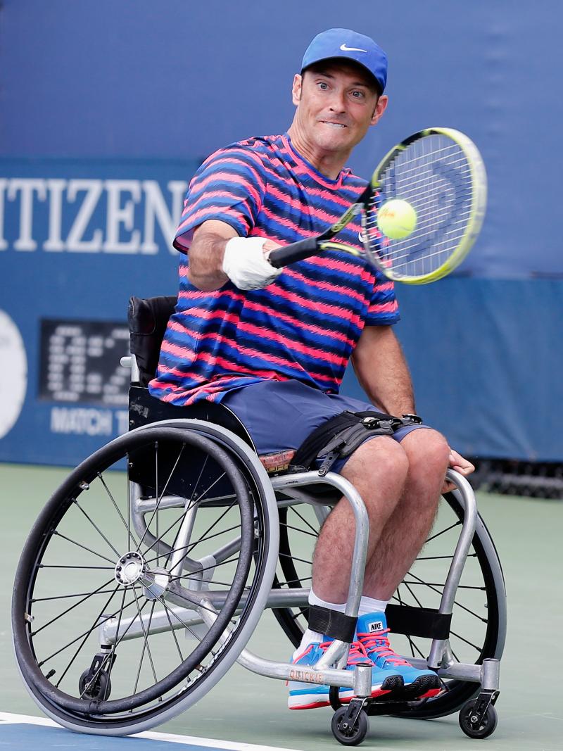 Man in wheelchair with tennis racket on the field.