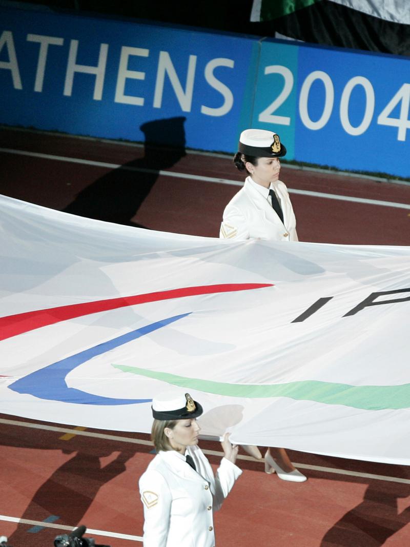 Six people carry a flag with the Paralympic symbol into a stadium