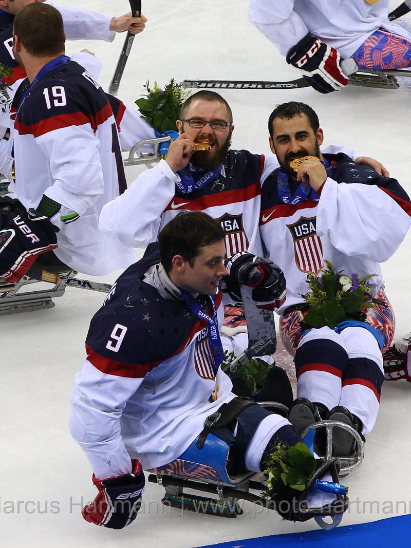 Four sledge hockey player on the ice, posing for a camera with their gold medals
