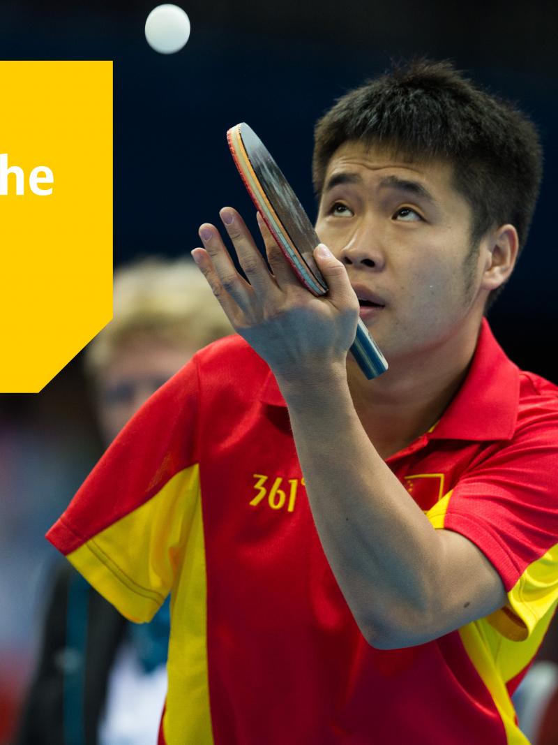 A one-armed Chinese table tennis player about to serve, watching the ball.