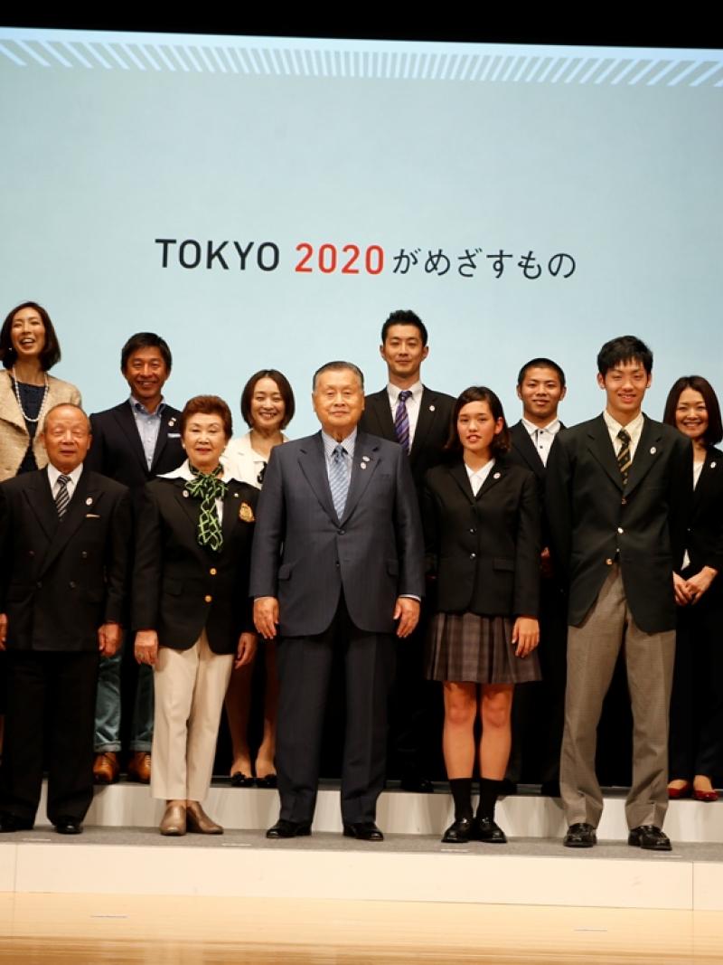 Japanese people standing in a line under a Tokyo 2020 banner