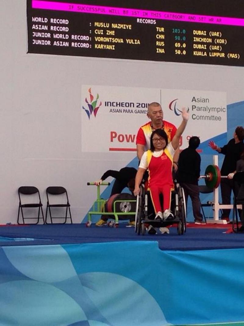 Women in wheelchair waving in front of a bench press