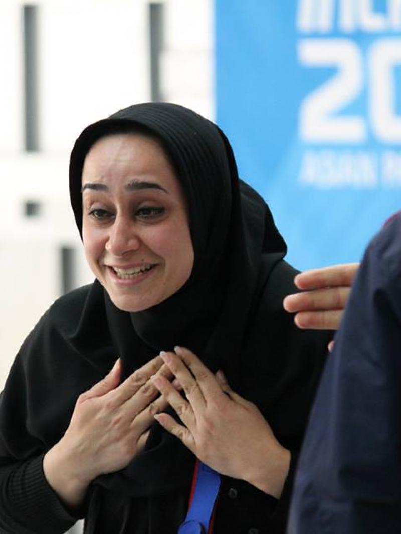 Women wearing a headscarf looks surprised and happy in front of a Incheon 2014 Asian Para Games banner