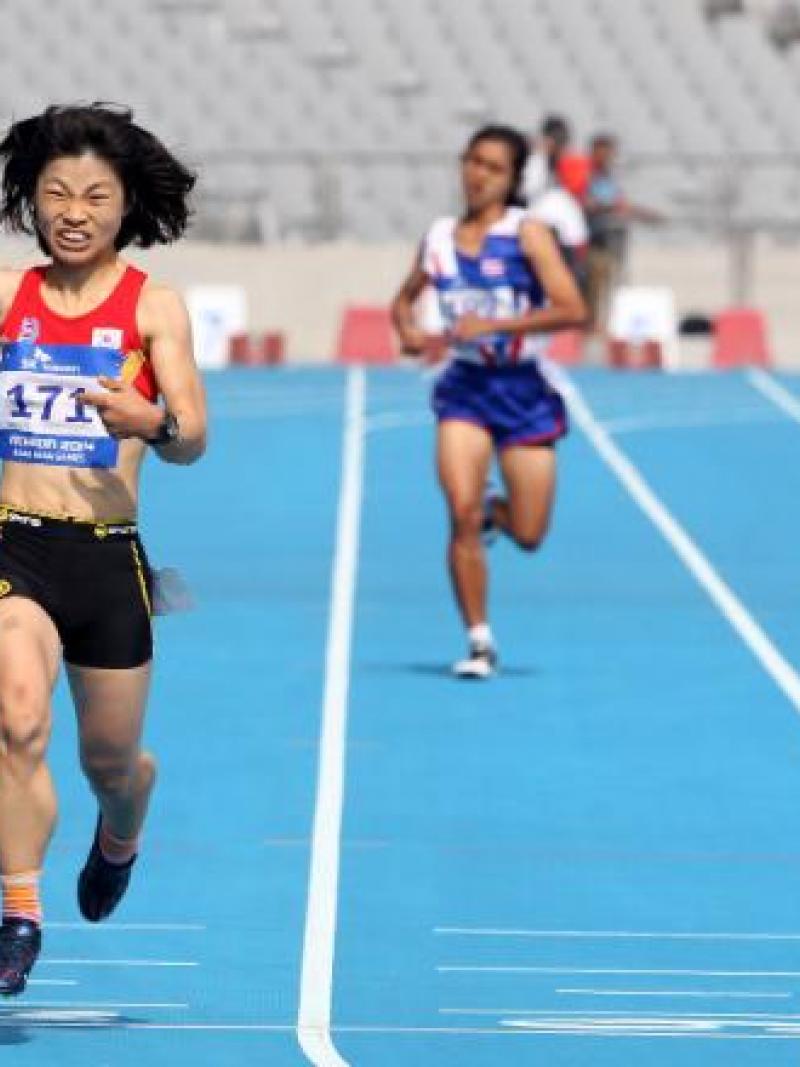 Female runner crosses the finish line on a blue track in a stadium, celebrating