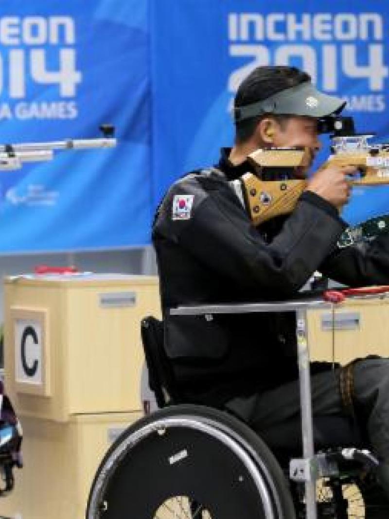 Two people in a shooting range, sitting in wheelchairs and targetting