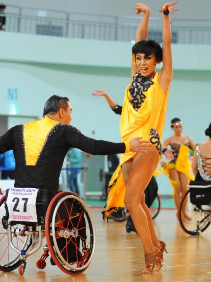 Man in wheelchair and women in dancing costumes doing an emotional latin dance move on the dance floor