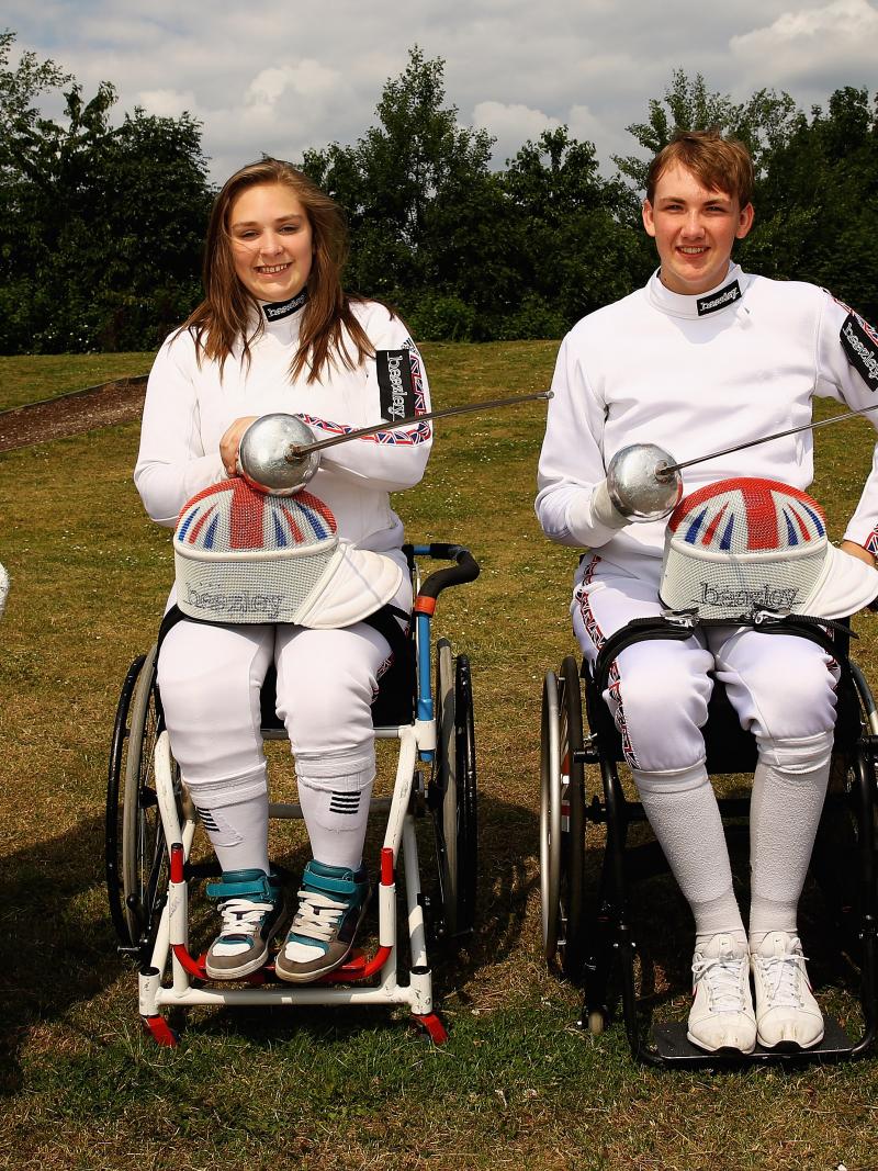 Four people in fencing suits and wheelchairs pose with their foils/epees