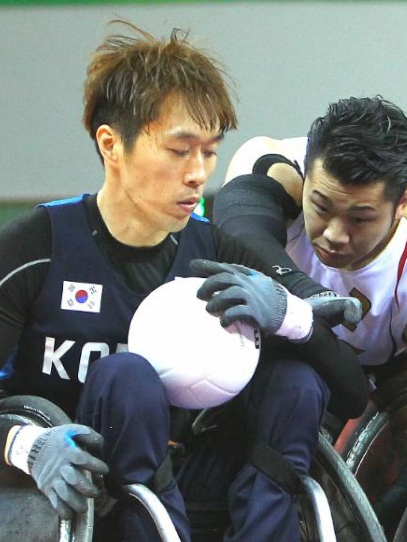 Two men in wheelchairs playing rugby, fighting for the ball