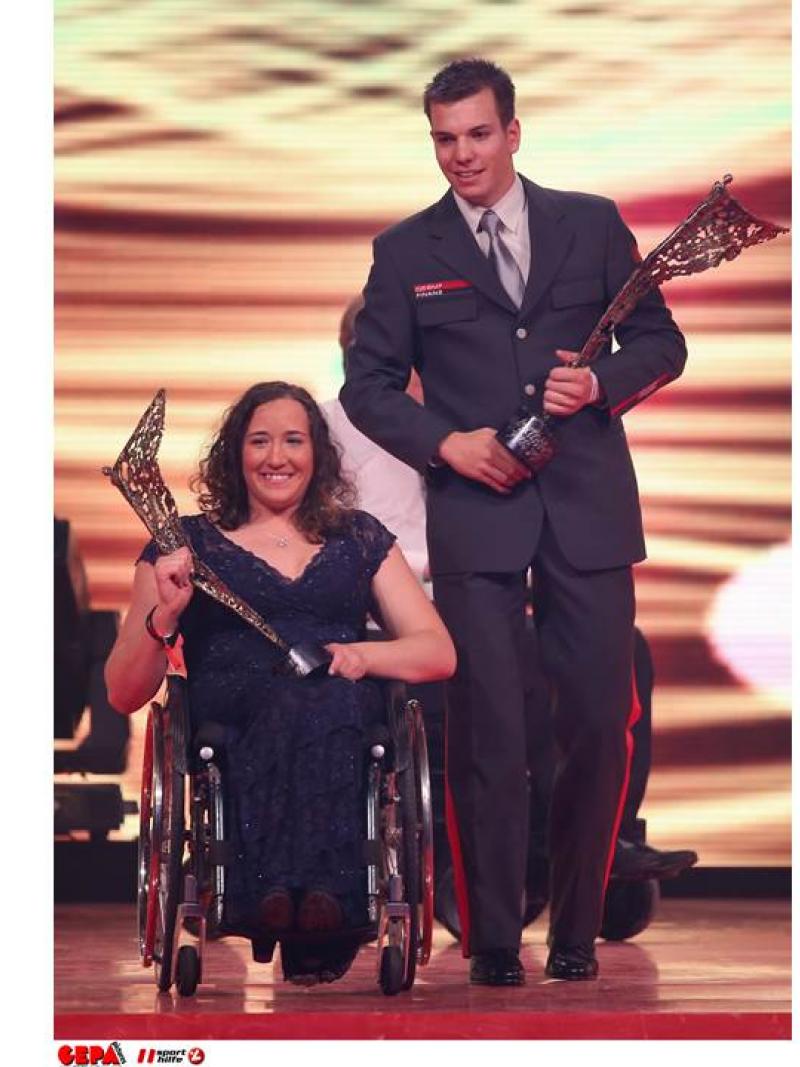 Women in wheelchair, man walking both holding a trophy in their hands
