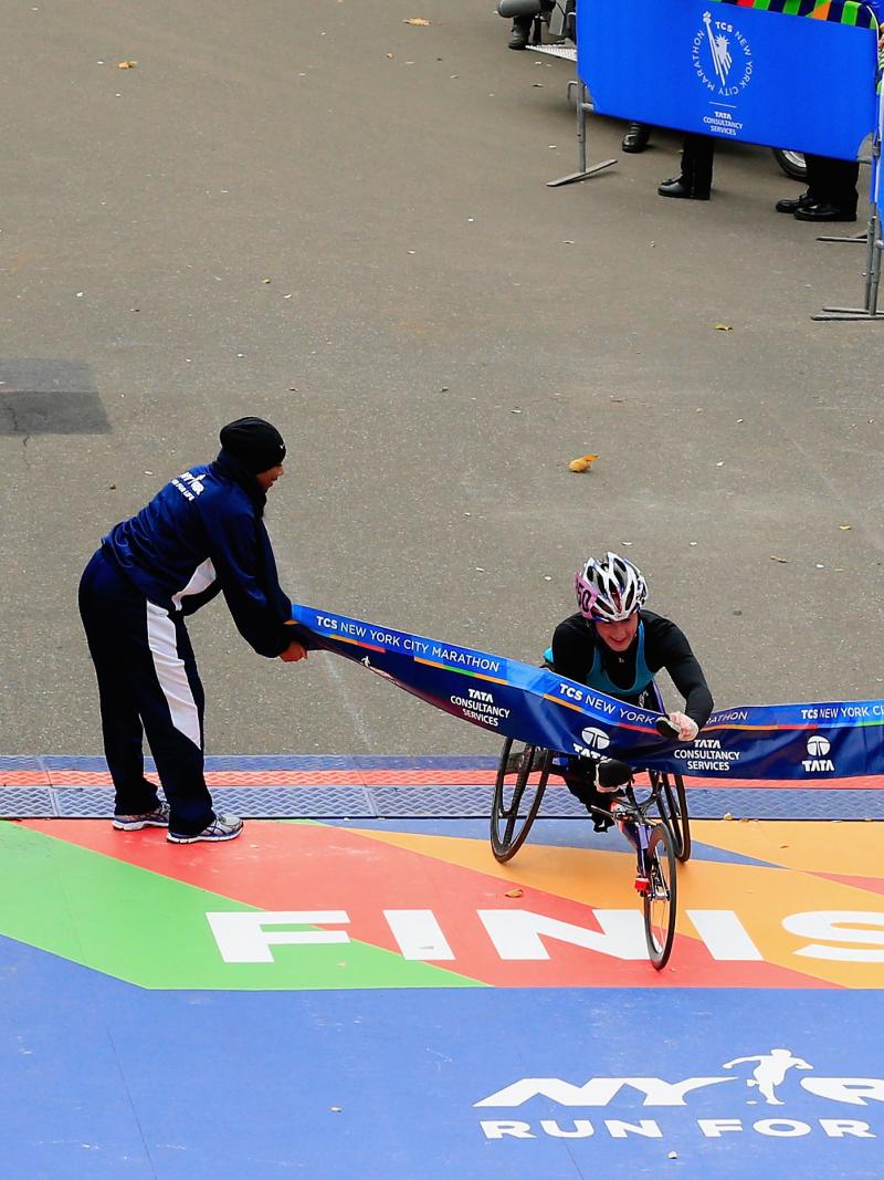 Women in racing wheelchair crosses the finish line on a street