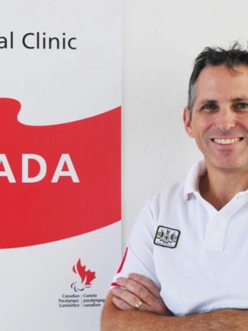 man looking at the camera with arms crossed in front of Canadian banner