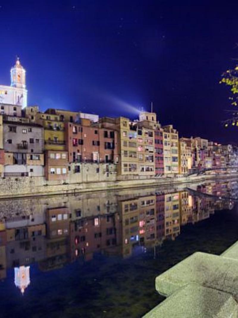 A night time shot of a river bank with stunning buildings in the background.