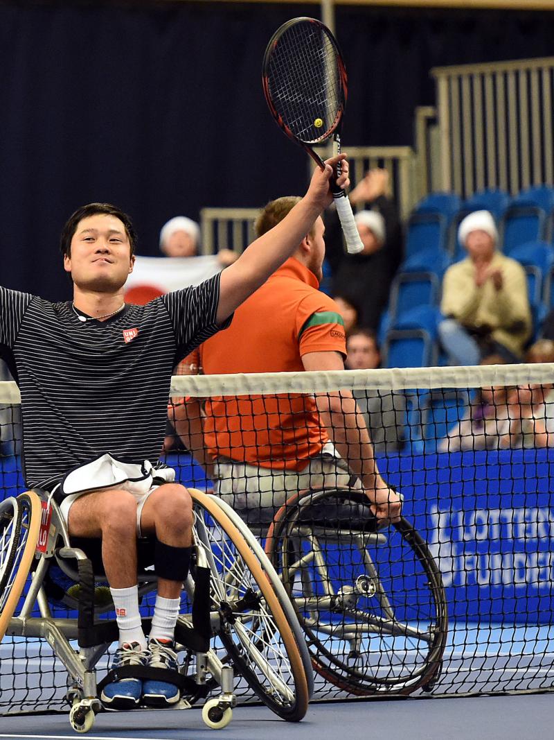 Man in wheelchair, holding tennis racket in triumphing pose