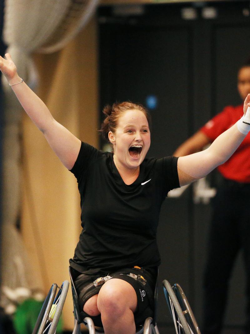 Women in wheelchair holding tennis racket, celebrating