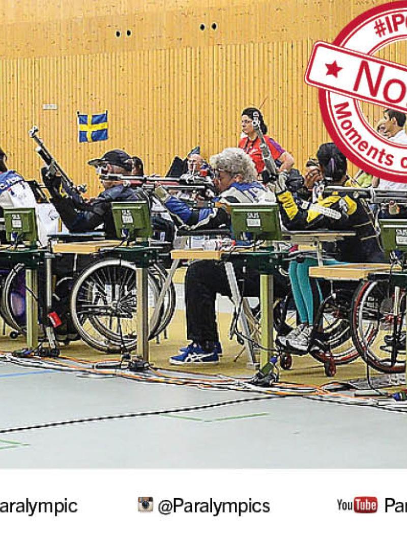 A line of seated athletes holding rifles line up for competition.
