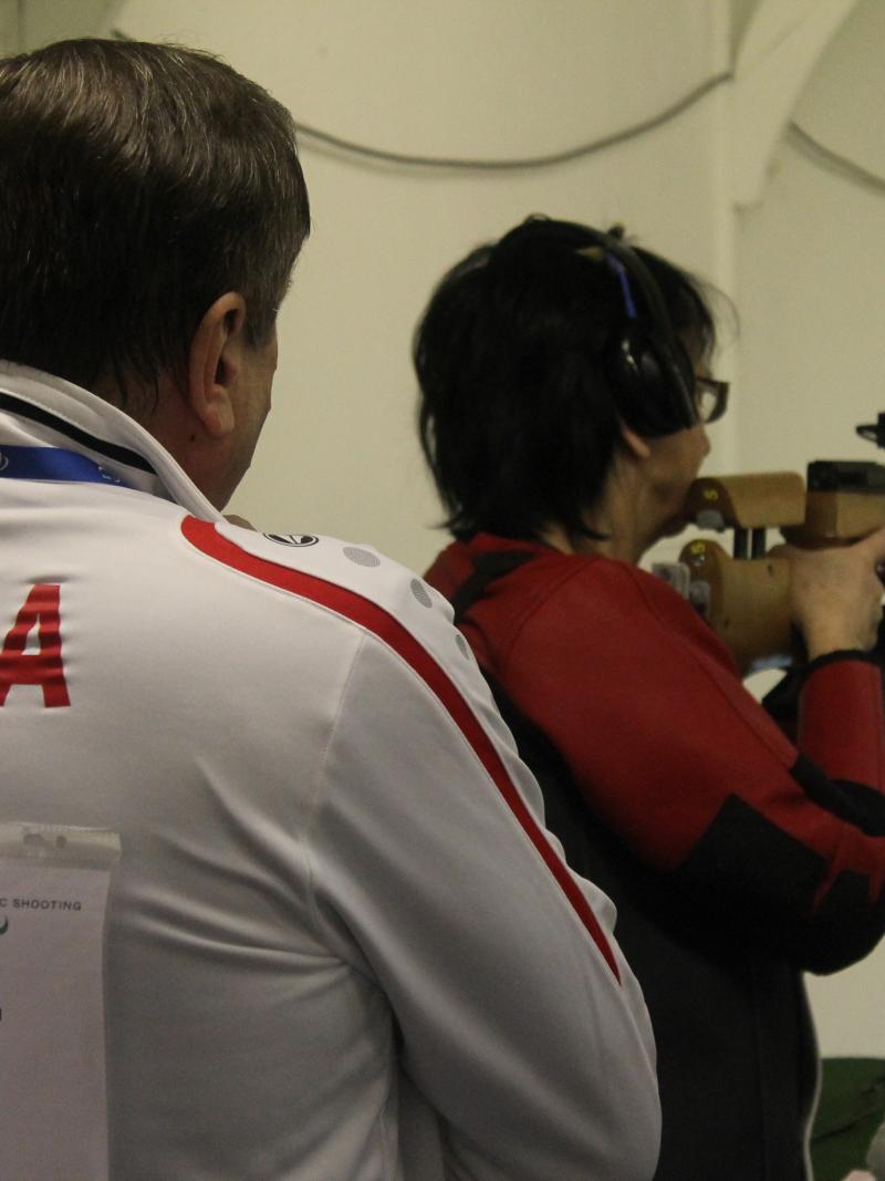 Women in a shooting range with a man standing behind her