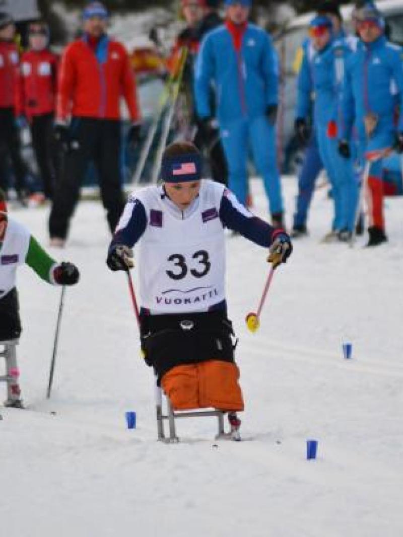 female athlete in a sit ski propelling herself forward