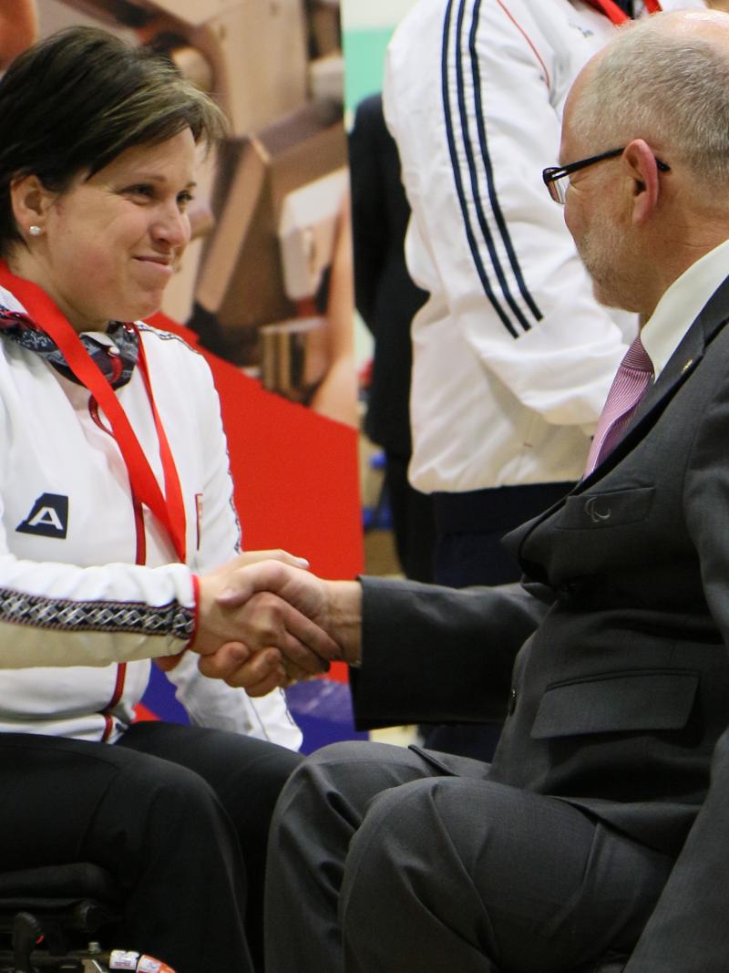 A female shooter in congratulated by a medal presenter