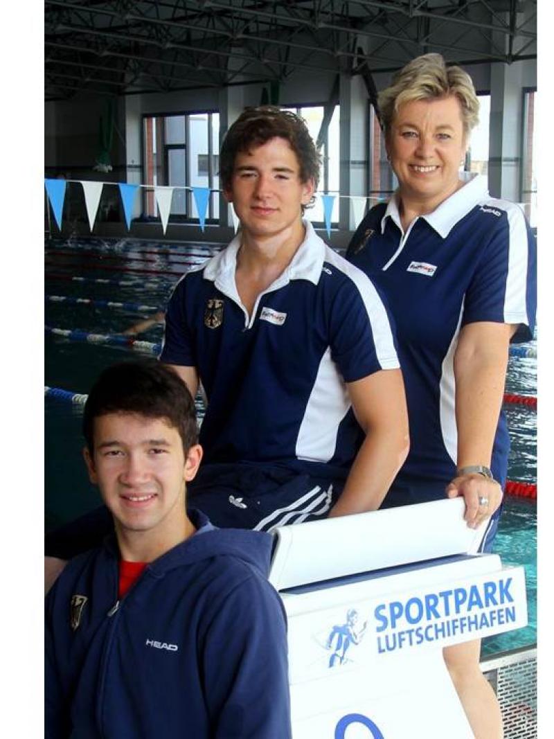 Two young boys and an adult woman pose in front of a swimming pool