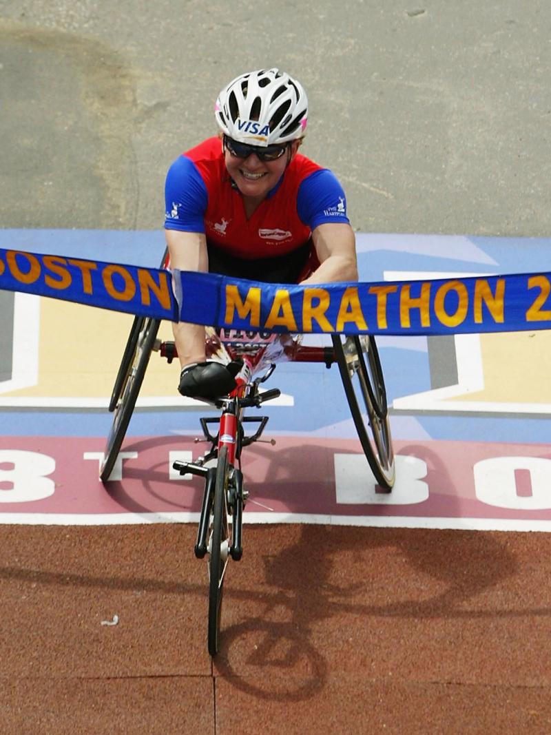 Women in racing wheelchair crosses a finish line