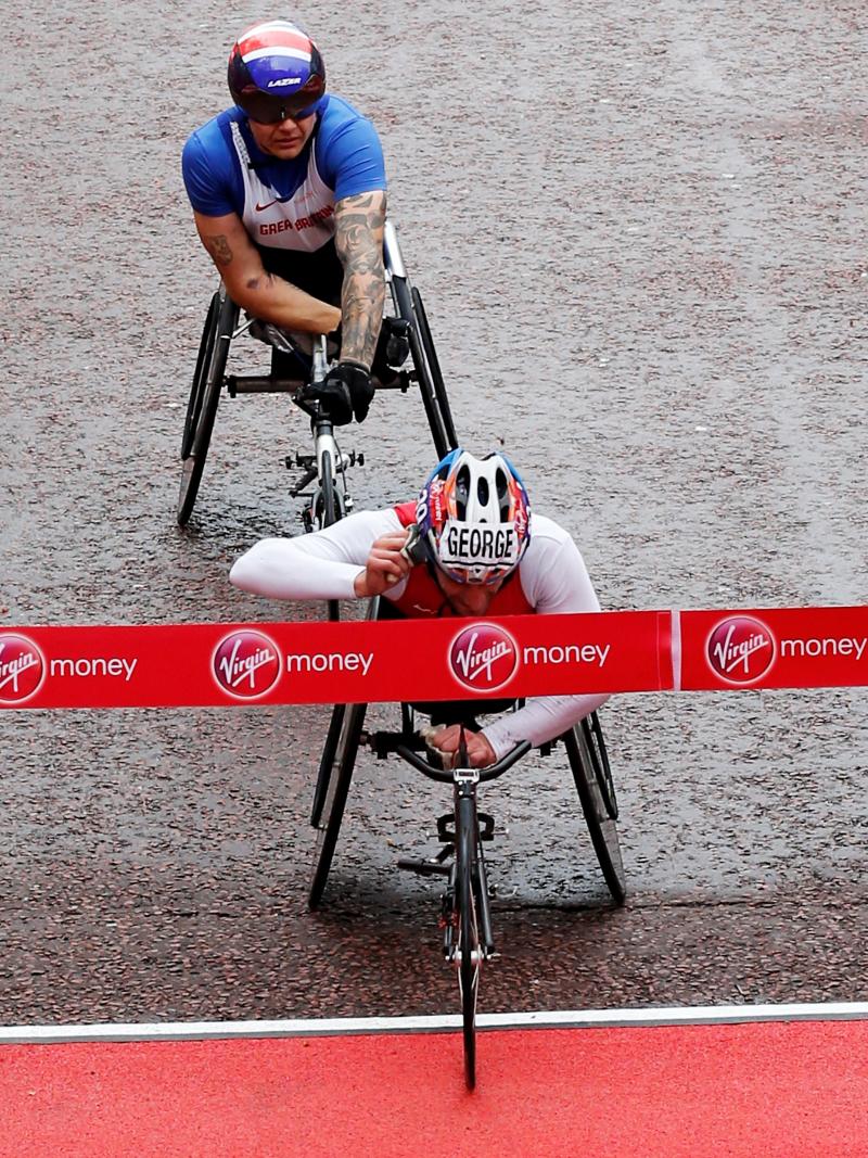 A wheelchair racer cuts through the finishing tape on a wet damp road.