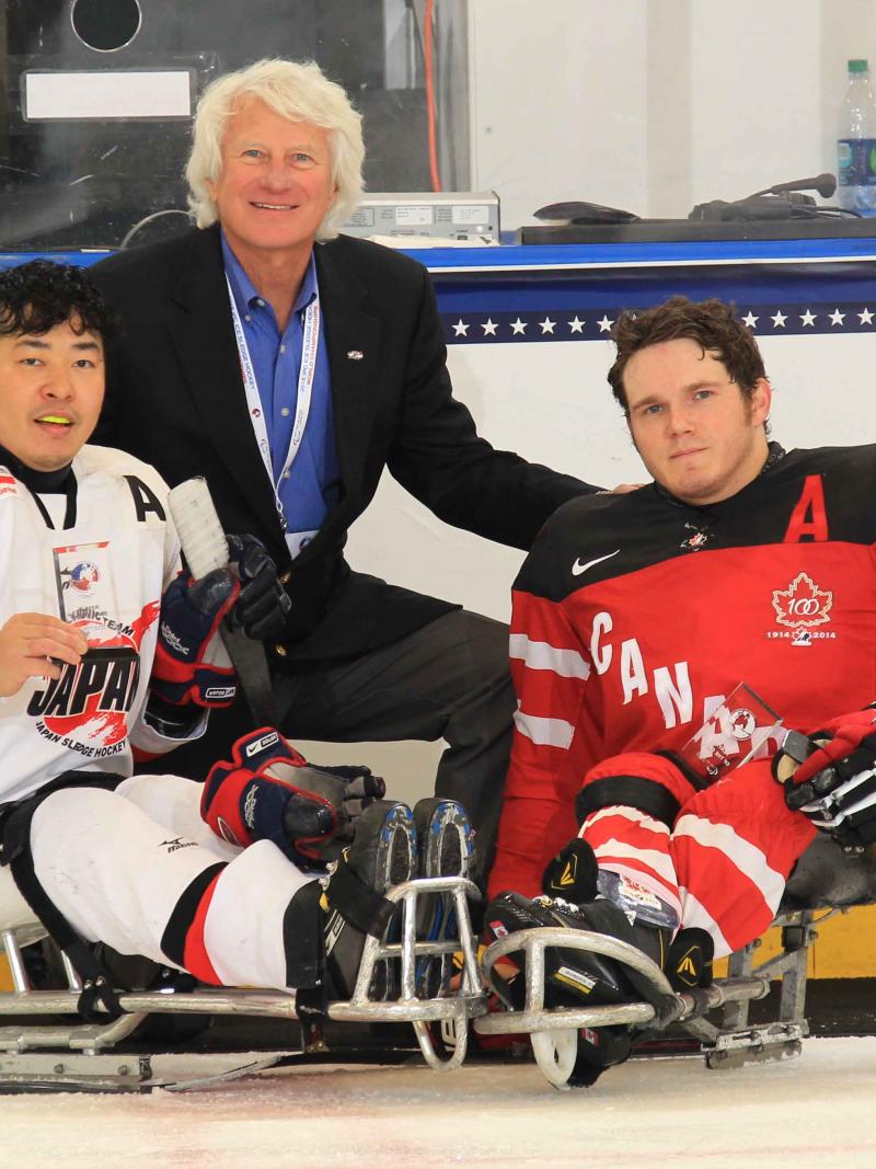 Two sledge hockey players and a man in a suit posing for the camera