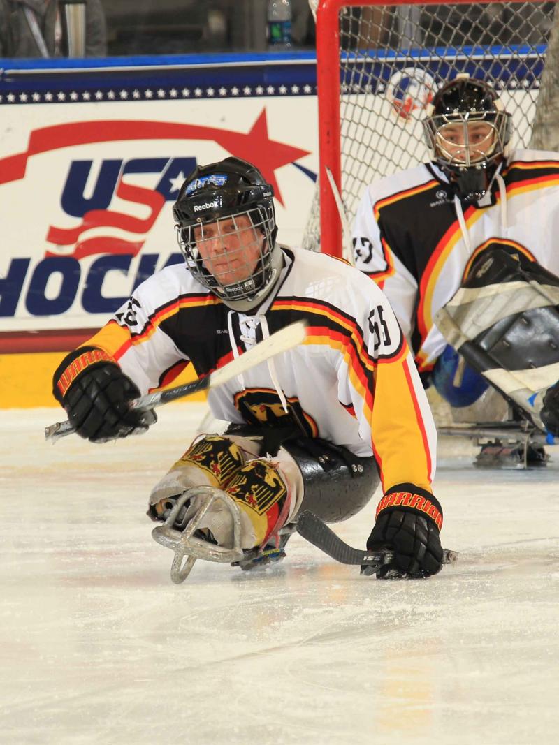 Two players on sledges on the ice, one focusing the puk