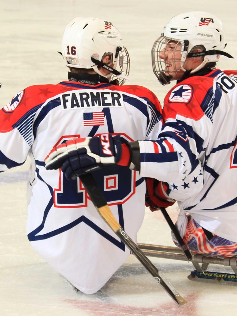 Two sledge hockey players on the ice, in a conversation