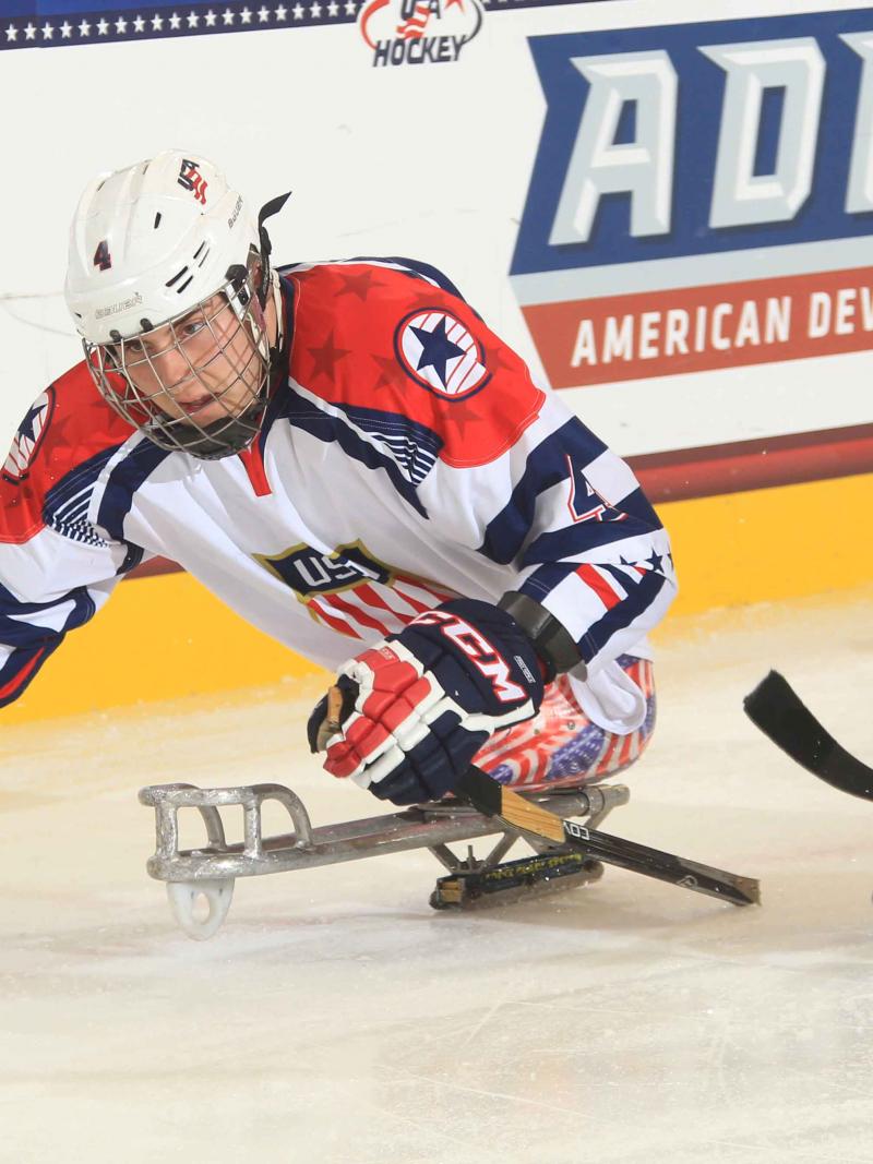 Two sledge hockey players chasing after the puck.