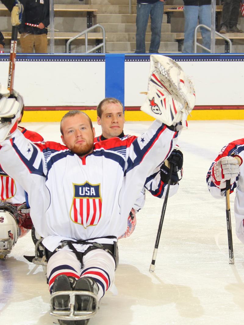 Sledge hockey players on the ice without their helmets, celebrating