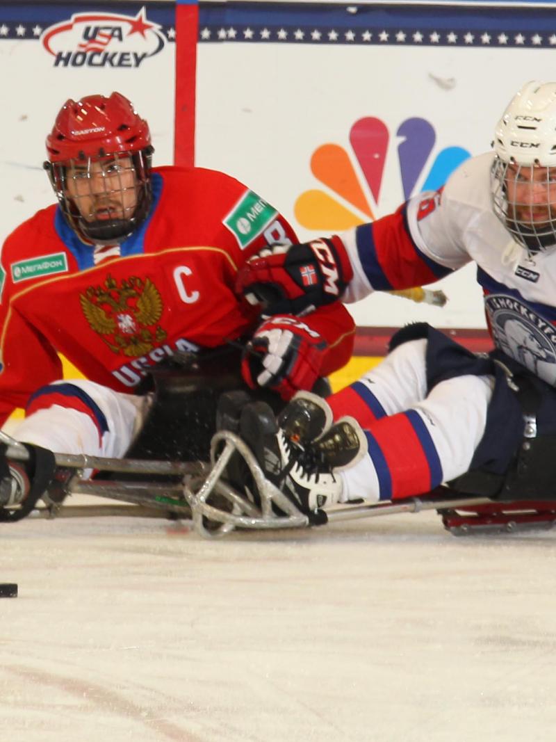 Two ice sledge hockey players chasing after the puck.