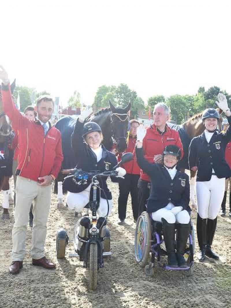 Group shot of seven people and horses in the background, waving to the camera