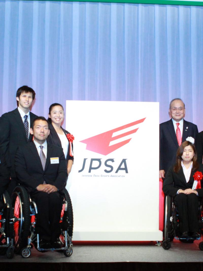 Group shot of around 20 people standing and in wheelchairs with a big banner