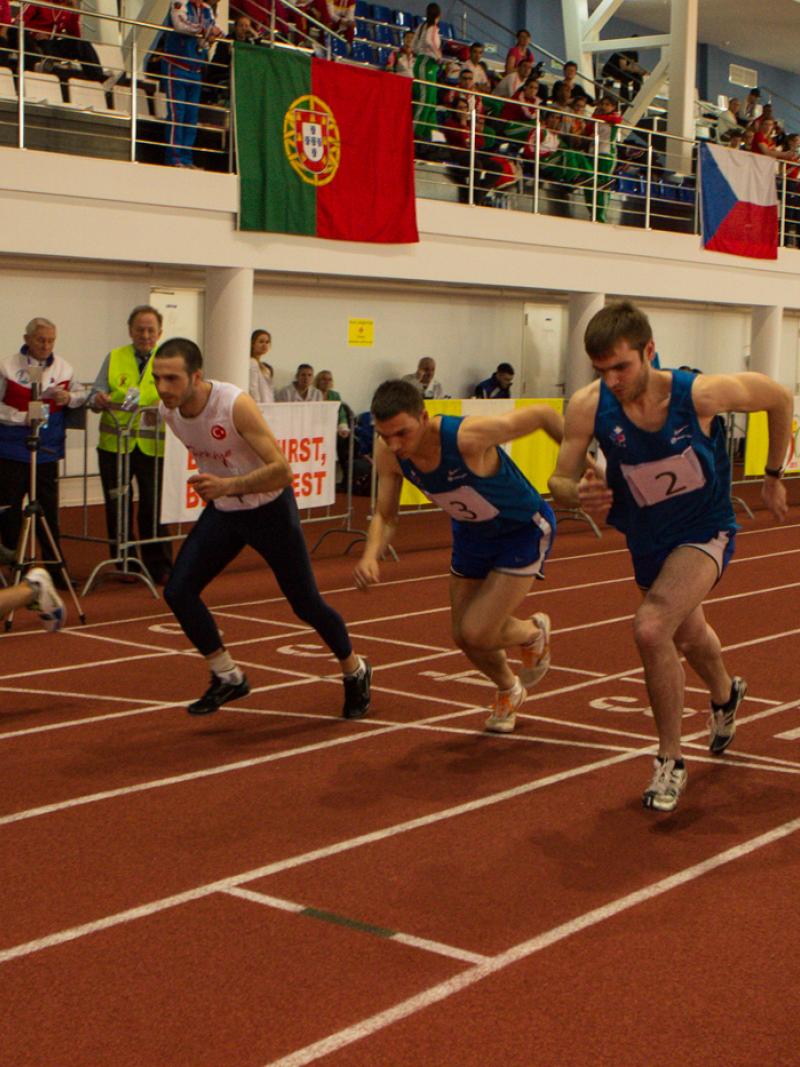 Five young men run on an athletics track next to each other