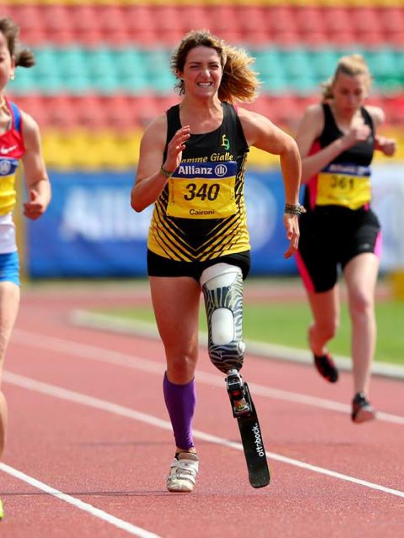 A woman with a running blade clenches her face in effort as she sprints forward.
