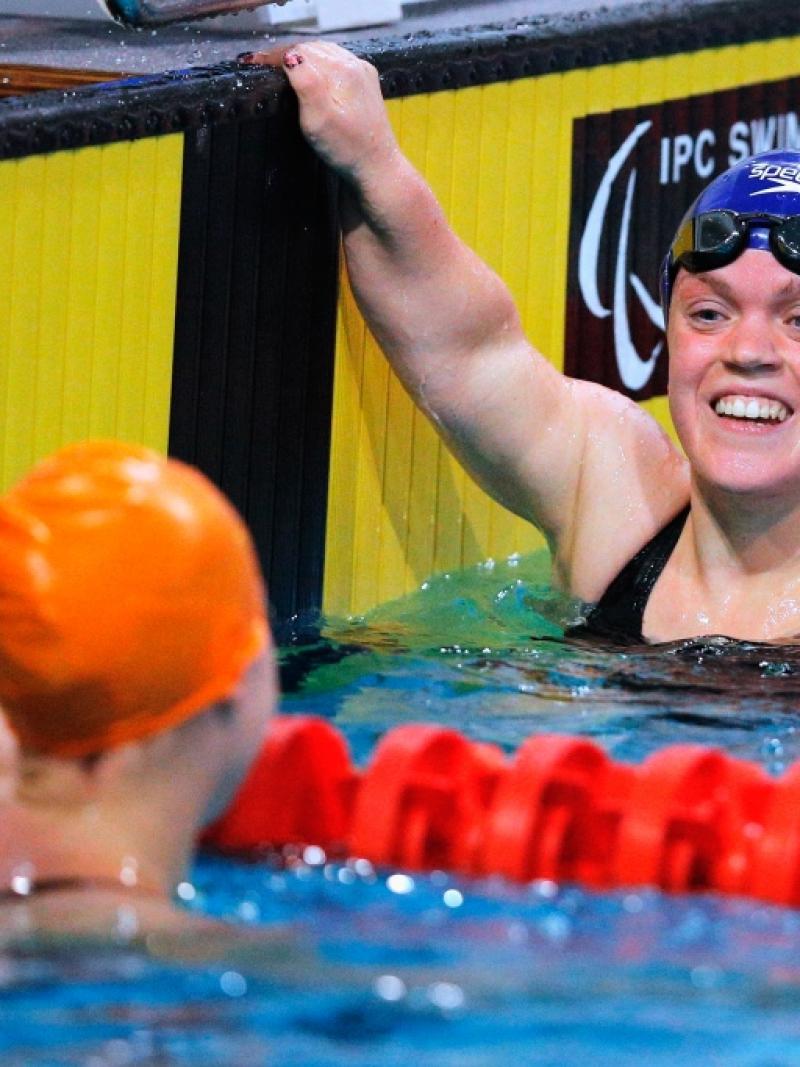 Two women smiling at each other in a swimmig pool after a race