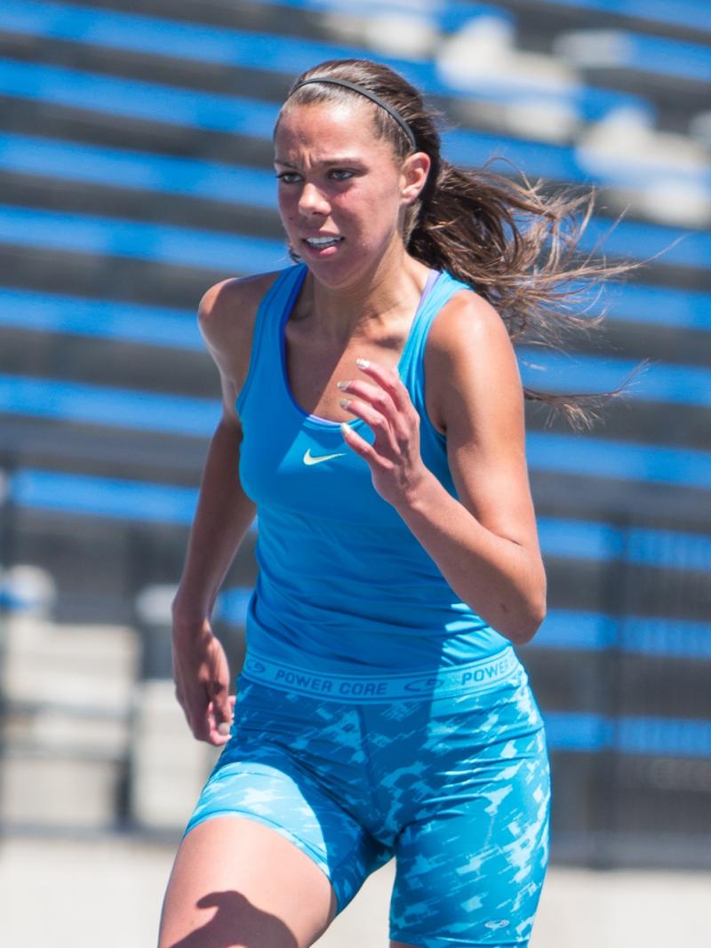 Women runs on a blue track, looks focused