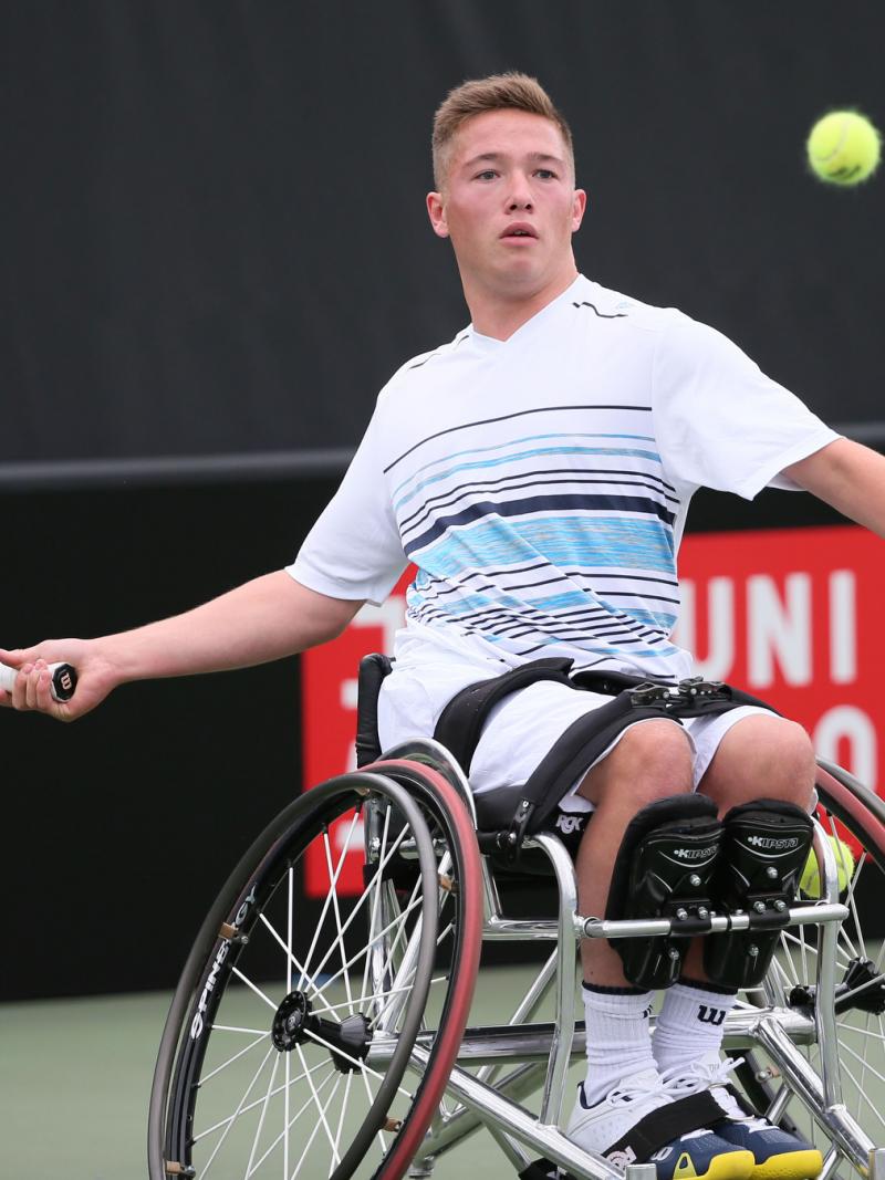 Wheelchair tennis player hits a ball back.