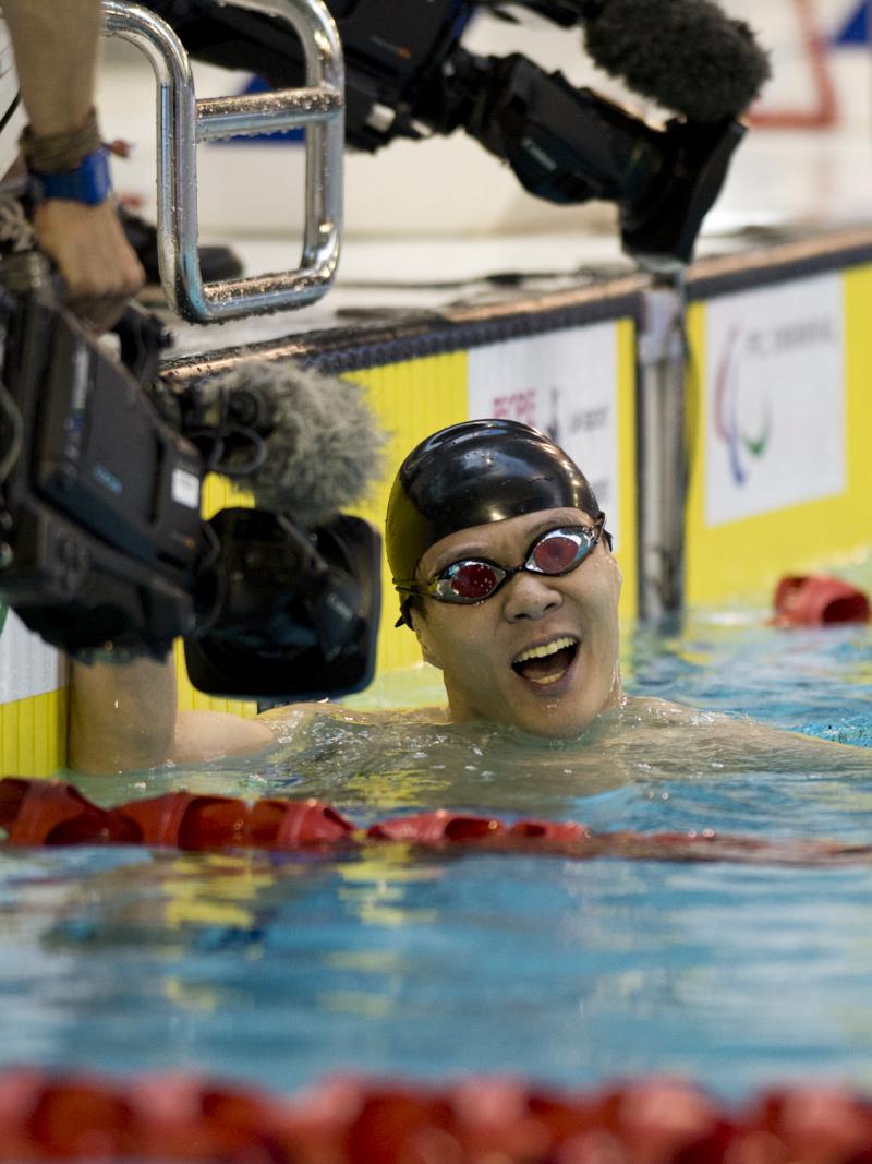 Man in swimming pool, celebrating after finishing a race. Camera filming him.