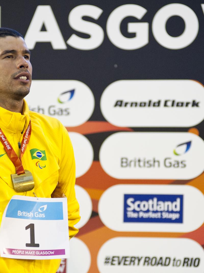 Man in yellow jacket standing ona podium, wearing a gold medal
