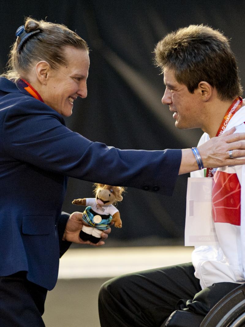 Man in wheelchair on the podium receiving a medal from a woman