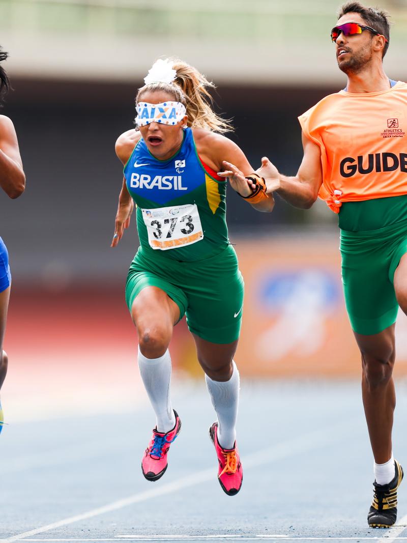 blindfolded runner with guide and another female runner crossing a finish line